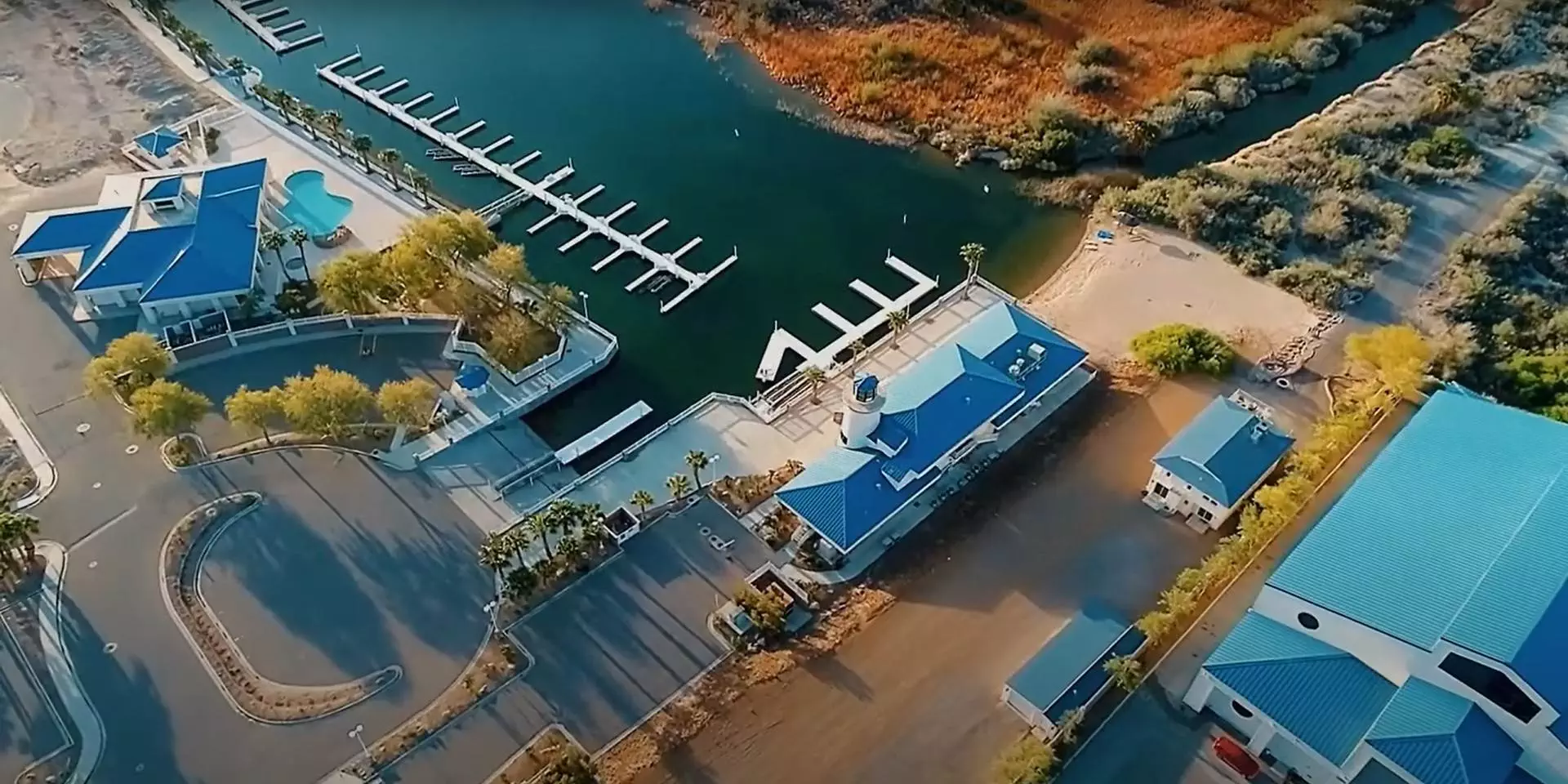 Aerial view of Laughlin Lagoon with blue-roofed buildings, a section of docked marina, and surrounding greenery.